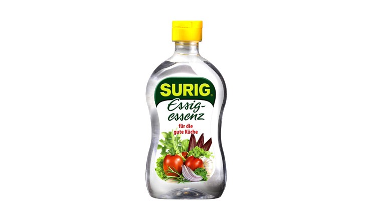 Eine transparent durchsichtige Flasche SURIG Essigessenz mit gelbem Deckel und Abbildung von Tomaten, Zwiebeln sowie Kräutern auf dem Etikett.