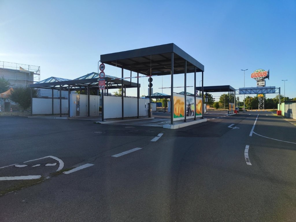 Ein leerer Parkplatz mit Überdachung, GLOBUS Logo im Hintergrund, klare Fahrbahnmarkierungen und aufgehängte Verkehrsschilder.