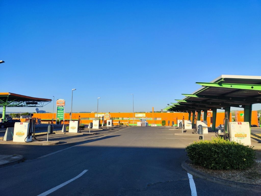 Mehrere Zapfsäulen an einer GLOBUS Tankstelle mit grünen und orangen Überdachungen unter blauem Himmel.