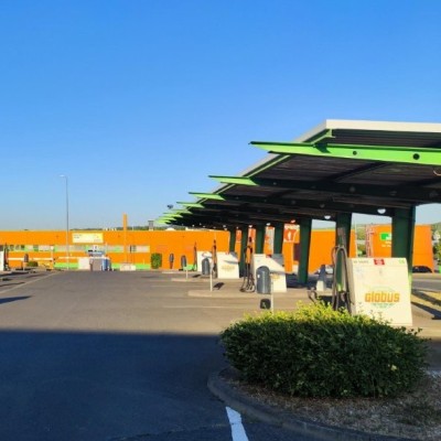 Mehrere Zapfsäulen an einer GLOBUS Tankstelle mit grünen und orangen Überdachungen unter blauem Himmel.