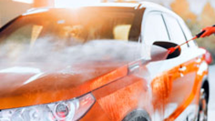 Ein orangefarbenes Auto wird mit einem Wasserstrahl in einer Waschanlage gereinigt.