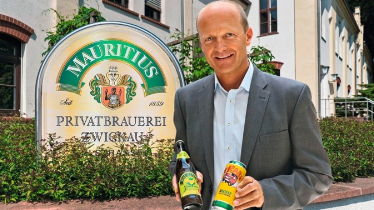 Ein Mann im Anzug hält eine Bierflasche und eine Bierdose vor dem Schild der Mauritius Privatbrauerei Zwickau.