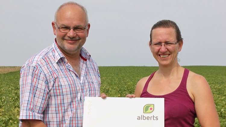 Zwei Personen halten ein Schild mit der Aufschrift „alberts … wir bauen an für purvegan! natürlich, biologisch, gentechnikfrei“.