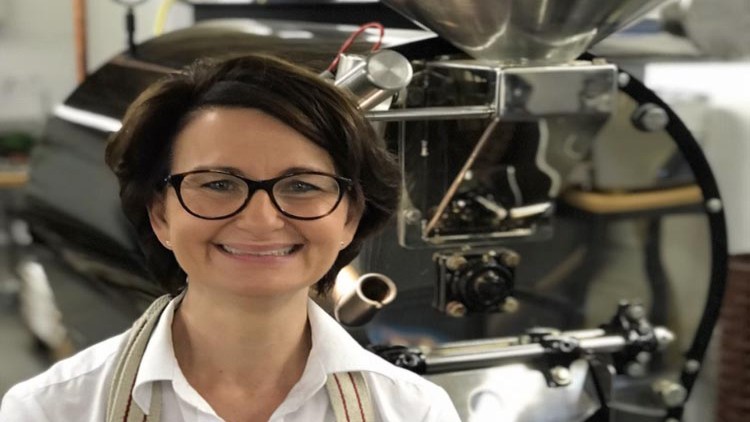 Eine silberne Kaffeeröstmaschine mit glänzenden Oberflächen und technischen Bedienelementen steht in einem Raum.