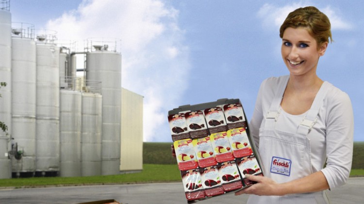 Person in weißer Kleidung hält eine Verpackung mit mehreren Frischli-Dessertbechern, im Hintergrund stehen silberne Tanks.