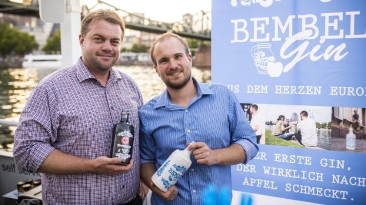 Zwei Personen halten Flaschen mit Gin vor einem Banner mit der Aufschrift „Bembel Gin, aus dem Herzen Europas“.