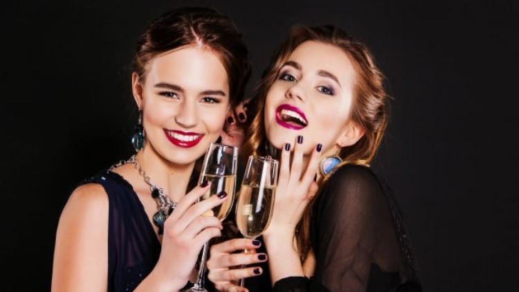Zwei Personen in eleganter Abendkleidung halten Gläser mit Sekt vor einem schwarzen Hintergrund.