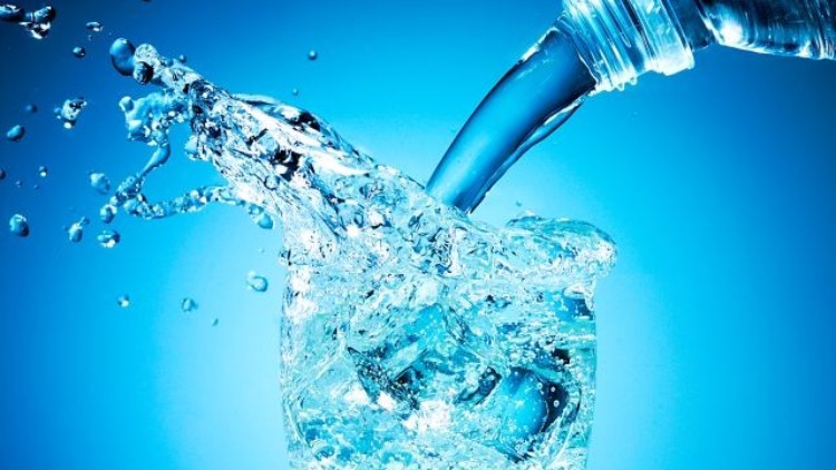 Wasser wird aus einer Flasche in ein Glas gegossen, während Wassertropfen und Spritzer in die Luft fliegen.