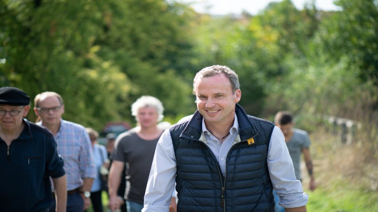 Gruppe von Menschen spaziert auf einem Weg durch eine grüne Landschaft bei sonnigem Wetter.