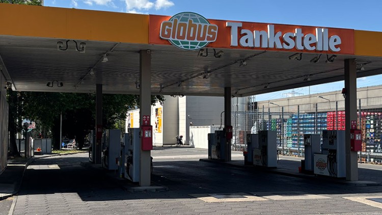 GLOBUS Tankstelle mit sechs Zapfsäulen, oranger Überdachung und der Aufschrift „Tankstelle 24 Stunden geöffnet“.