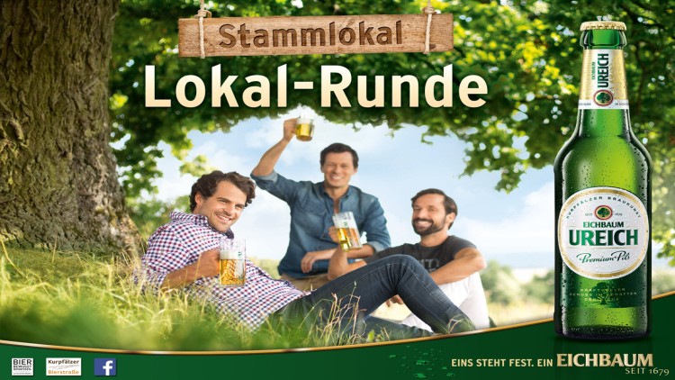 Gruppe sitzt unter einem Baum auf einer Wiese mit Biergläsern, Schriftzug „Stammlokal Lokal-Runde“ und Flasche „Eichbaum Ureich“.
