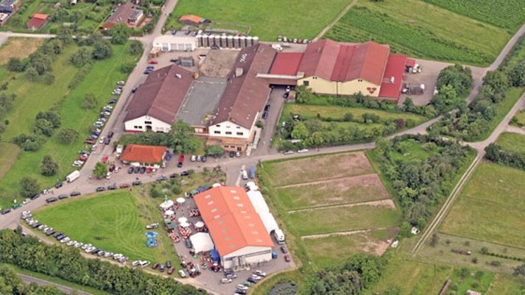 Eine landwirtschaftliche Anlage mit mehreren großen Gebäuden und Feldern in grüner Umgebung aus der Luftperspektive.