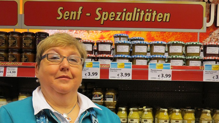Person hält drei Gläser mit Marmelade oder Senf vor einem Regal in der Abteilung für Senf-Spezialitäten im Supermarkt.