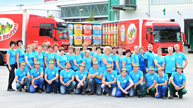 Eine Gruppe von Personen in blauen T-Shirts posiert vor zwei roten Lastwagen mit Aufdruck der Marke Bautzner.
