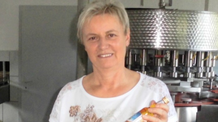 Person hält eine kleine Flasche mit gelbem Inhalt, im Hintergrund eine silberne Abfüllanlage und viele weitere Flaschen.
