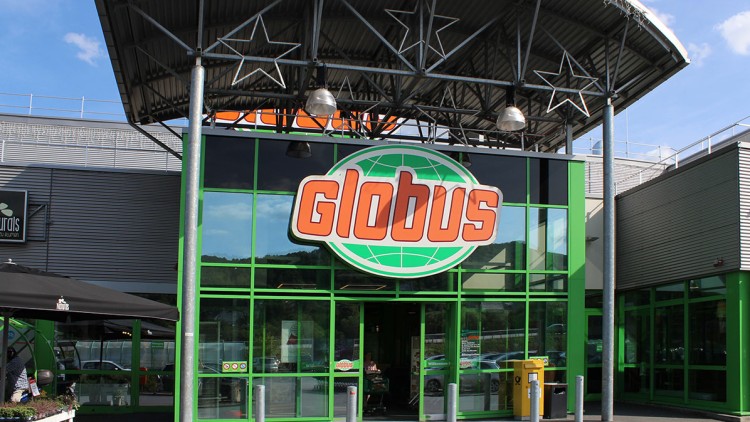 Der Eingang eines GLOBUS Marktes mit grünem Rahmen, einem großen GLOBUS-Logo und einem Überdach mit Sternendekoration.