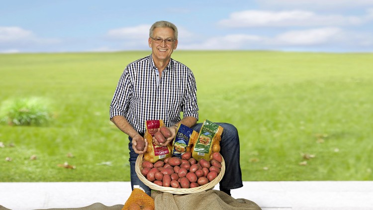 Ein Korb mit roten Kartoffeln, Kartoffelprodukten in Tüten und ein Netz mit gelben Kartoffeln vor einer grünen Wiese.