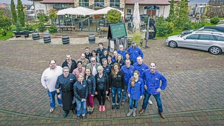 Gruppe von Menschen in Arbeitskleidung steht auf einem gepflasterten Platz vor einem Gebäude mit Steinfassade und Glasfenstern.