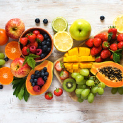 Verschiedene frische Früchte wie Papaya, Mango, Trauben, Erdbeeren, Orangen und Äpfel auf einem hellen Holzuntergrund.