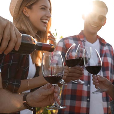 Eine Hand schenkt roten Wein aus einer Flasche in ein Glas ein, während andere Personen gefüllte Weingläser halten.