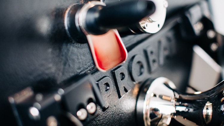 Schwarze Metallfläche mit erhabenem Schriftzug „PROBAT“, roter Griff und silberne Maschinenelemente im Detail.