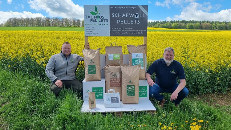 Mehrere braune Papiersäcke mit der Aufschrift „Taunus Pellets“ stehen vor einem gelben Blumenfeld, daneben ein Schild mit Infos.