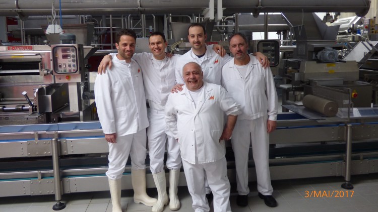 Fünf Personen in weißer Arbeitskleidung stehen in einer industriellen Produktionshalle mit Förderbändern und Maschinen.