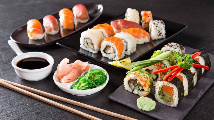 Verschiedene Sushi-Rollen und Nigiri auf Tellern mit Sojasauce, eingelegtem Ingwer, Algensalat, Wasabi und Essstäbchen.