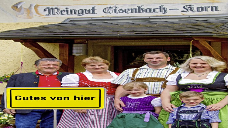 Sechs Personen in traditioneller Tracht vor einem Gebäude mit dem Schild „Gutes von hier“ und der Aufschrift „Weingut Eisenbach-Korn“.