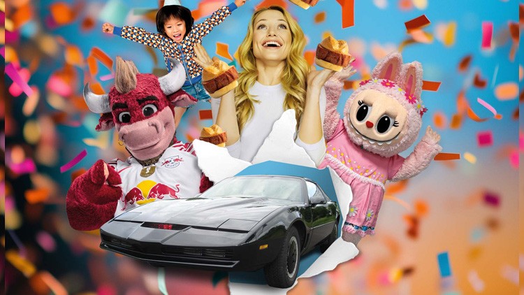 Auto mit schwarzer Lackierung steht vor buntem Hintergrund, flankiert von zwei Maskottchen sowie einer Person mit Kuchen in den Händen.