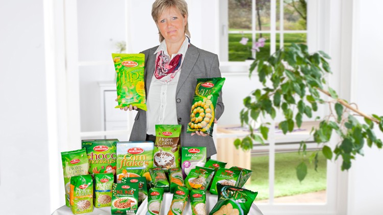 Auf einem weißen Tisch stehen verschiedene grüne Verpackungen von Lebensmitteln der Marke Müller’s Mühle vor einem Fenster.