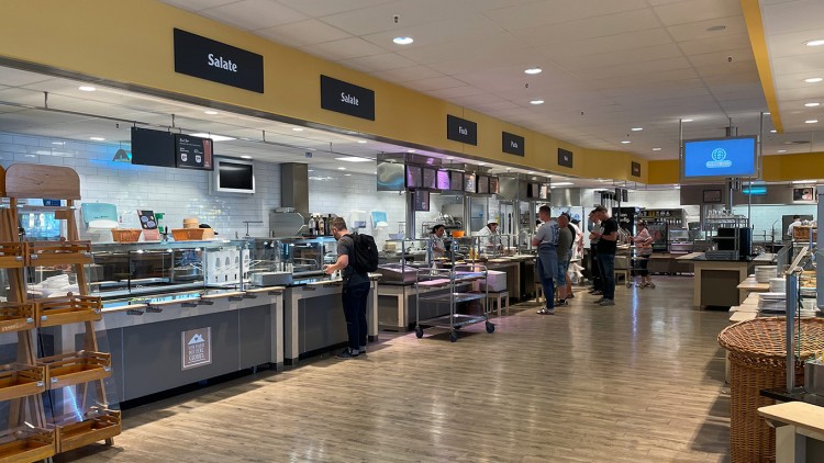 Mehrere Personen stehen in einer Selbstbedienungstheke eines GLOBUS Restaurants mit Schildern wie „Salate“ und „Fisch“.