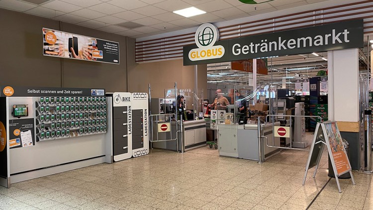 Eingangsbereich des GLOBUS Getränkemarkts mit „Scan & Go“-Station, Ladestation für E-Bikes und mehreren Kassen.
