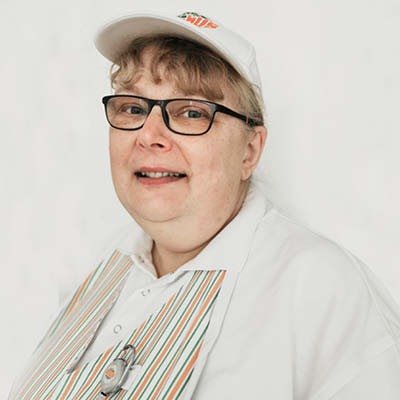 Person in weißem Poloshirt, gestreifter Schürze und weißer Kappe mit GLOBUS Logo vor weißem Hintergrund.