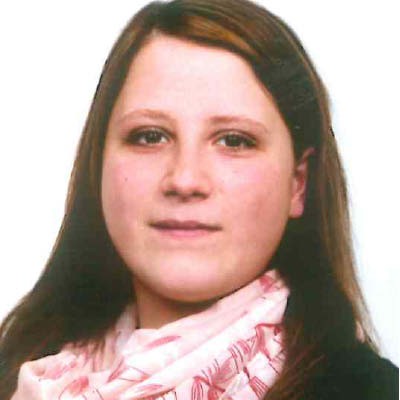 Person mit schulterlangem braunem Haar trägt einen weißen Schal mit rosa Muster vor neutralem Hintergrund.