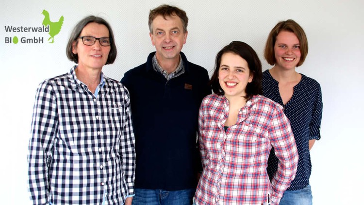 Vier Personen stehen vor einer weißen Wand, links oben ist das Logo der Westerwald BIO GmbH mit grünem Hahn sichtbar.