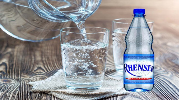 Ein Glas wird mit sprudelndem Mineralwasser aus einem Krug gefüllt, daneben steht eine Rhenser-Wasserflasche mit Kohlensäure.