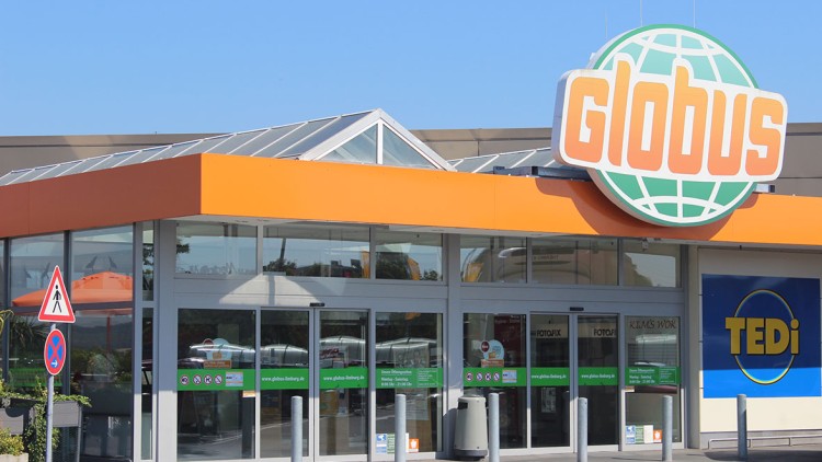 Eingangsbereich eines GLOBUS Markts mit orange-grünem Logo über der Tür, daneben ein TEDi-Schriftzug auf blauem Hintergrund.