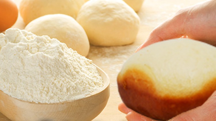 Mehrere Teigkugeln auf bemehlter Fläche, eine Hand hält gebräunten Teig, daneben Holzschale mit Mehl und ein Ei.