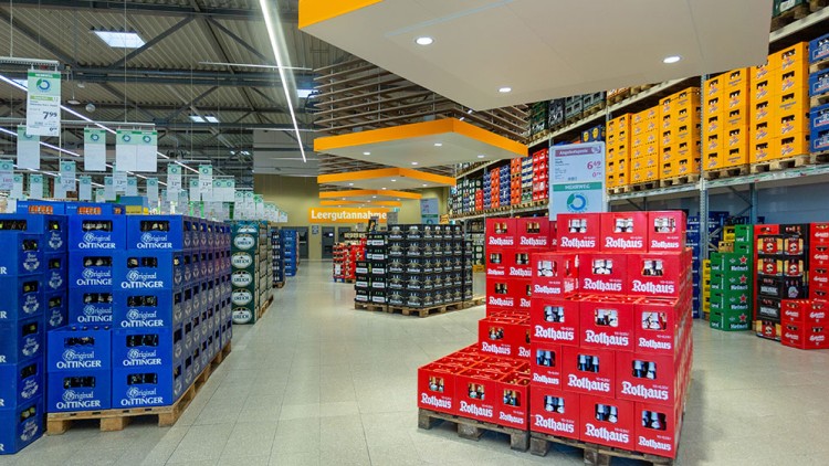 Ein Getränkemarkt mit Kästen verschiedener Marken auf Paletten, darüber Preisschilder und ein Schild mit der Aufschrift „Leergutannahme“.