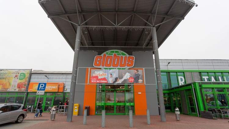 Eingangsbereich eines GLOBUS Marktes mit orangem Logo, Werbeplakat „Das wird mein Jahr“, grünen Türen und umliegenden Parkplätzen.
