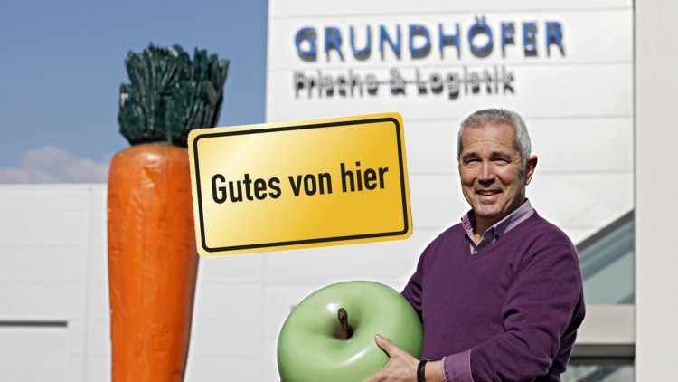 Große Karotten-Skulptur, gelbes Schild mit „Gutes von hier“ und Firmenschild „GRUNDHÖFER Frische & Logistik“ im Hintergrund.