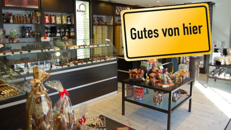 Ein Verkaufsraum mit Glasvitrinen voller Pralinen und Schokolade, im Vordergrund ein gelbes Schild mit der Aufschrift Gutes von hier.