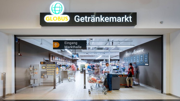 Eingang des GLOBUS Getränkemarkts mit Beschilderung „Eingang Markthalle“, Einkaufswagen und Personen an Selbstbedienungskassen.