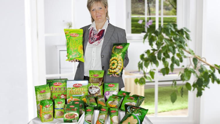 Eine Person präsentiert auf einem Tisch verschiedene grüne Verpackungen mit Lebensmitteln der Marke „Delhaize“.