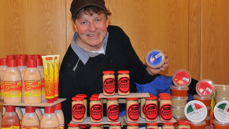 Mehrere Flaschen, Tuben und Gläser mit der Aufschrift „Feuer Sauce“ und anderen Saucen sind auf einem Tisch angeordnet.