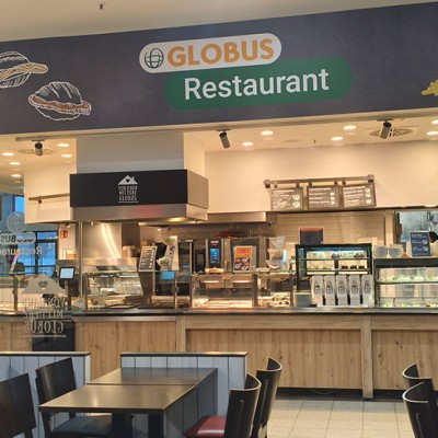 Theke mit Speisen hinter Glas im GLOBUS Restaurant unter einem Schild mit dem GLOBUS Logo und Speiseillustrationen.