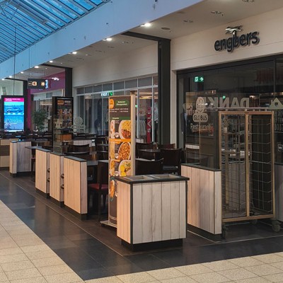 Sitzbereich des GLOBUS Restaurants in einer Einkaufspassage, daneben Geschäft „engbers“ und Werbetafel mit Rabattaktionen.