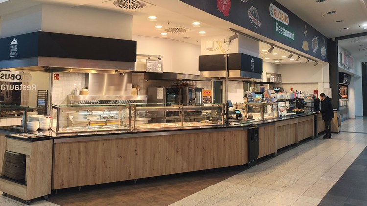 Großes Selbstbedienungsbuffet im GLOBUS Restaurant mit Theken aus Holz, Speisenbehältern, Tellern und Beleuchtung.