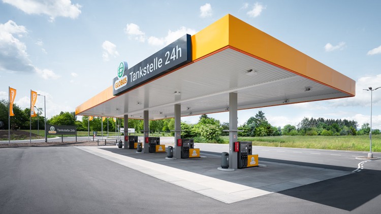 Die GLOBUS Tankstelle mit gelbem Dach und dem Schriftzug „Tankstelle 24h“ steht auf einem asphaltierten Gelände mit Zapfsäulen.